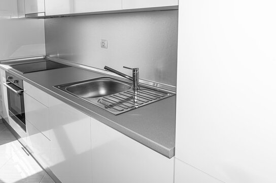 A modern minimalist kitchen features white cabinets, a stainless steel sink, and sleek built-in appliances.