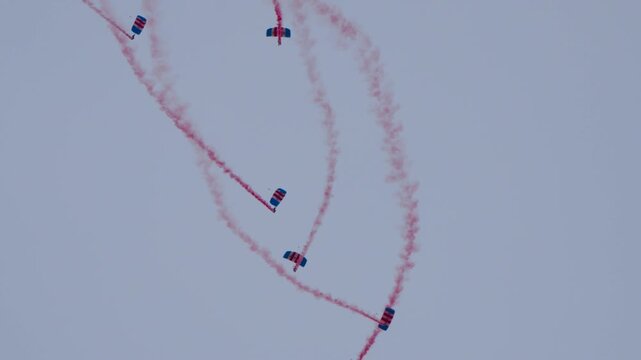 Parachute team with red smoke trails weaving in pattern through the sky