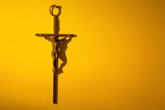 Metal crucifix hanging on a wall in warm yellow light with copy space.