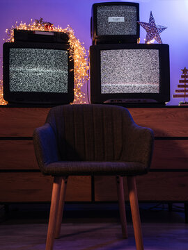 Empty chair in front of three retro CRT televisions showing static noise and no signal with Christmas decor