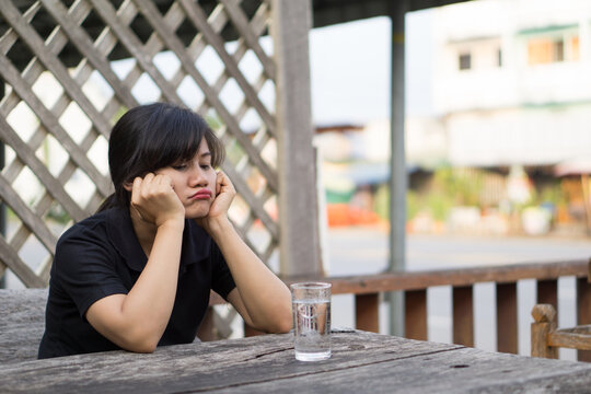 Bored Young Asian Woman Sitting Alone at Restaurant Table with Glass of Water