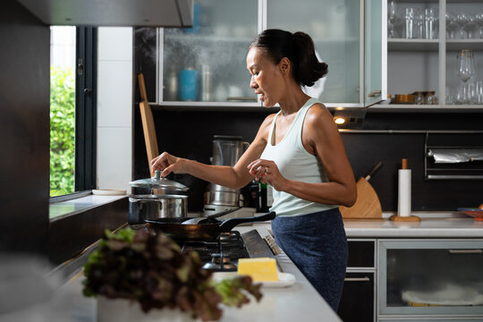 Healthy senior woman cooks at home beside a steaming pot in a modern kitchen. The authentic lifestyle scene represents nutritious meals, wellness, active aging, and everyday cooking.