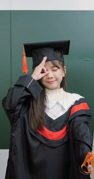 Happy Asian child in graduation gown holding scroll diploma.