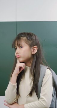 Thoughtful young schoolgirl touching cheek and looking up while thinking deeply.