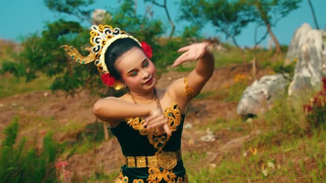 A medium shot of a female dancer in a green and gold costume executing precise and graceful hand gestures (mudras) characteristic of traditional Indonesian dance.