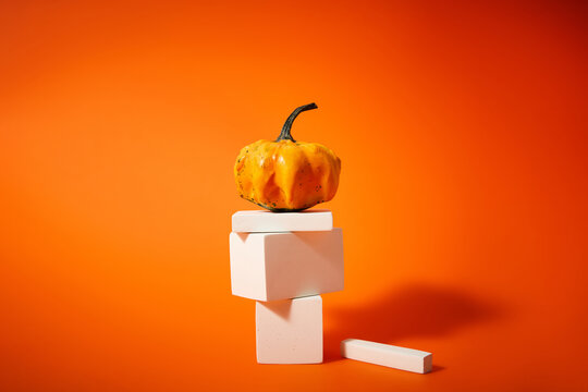 Small Decorative Pumpkin on Stacked White Geometric Pedestals on Orange Background