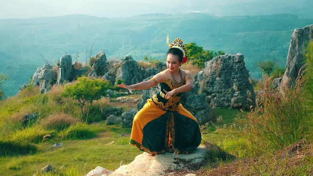 A full-body shot of a dancer maintaining a difficult squatting pose (tanjak duduk) on a rough limestone rock, wearing a vibrant traditional costume.