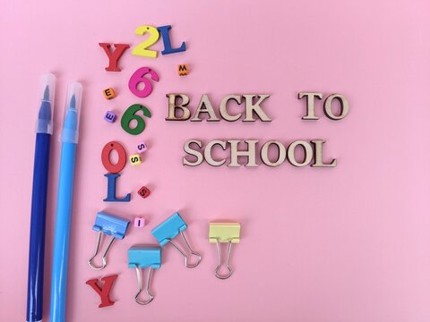 back to school background. Wooden letters spelling Back to School surrounded by colorful numbers, markers and binder clips on a bright pink surface.