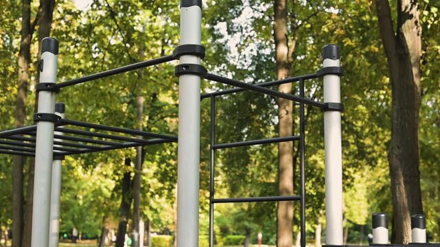 Outdoor fitness equipment is shown in a park setting, featuring monkey bars positioned among trees. The equipment is designed for physical exercise, showing clear structures for climbing and gripping