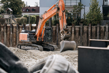Orange excavator with bucket at an urban residential construction site, surrounded by gravel, © Natalia Schuchardt