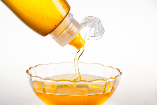 Golden Natural Honey Dripping from Squeeze Bottle into Clear Glass Bowl on Pure White Background