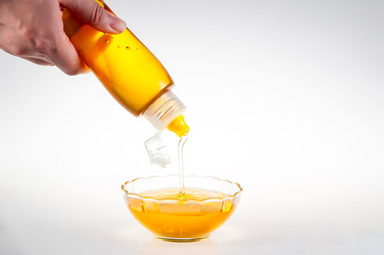 Golden Natural Honey Dripping from Squeeze Bottle into Clear Glass Bowl on Pure White Background