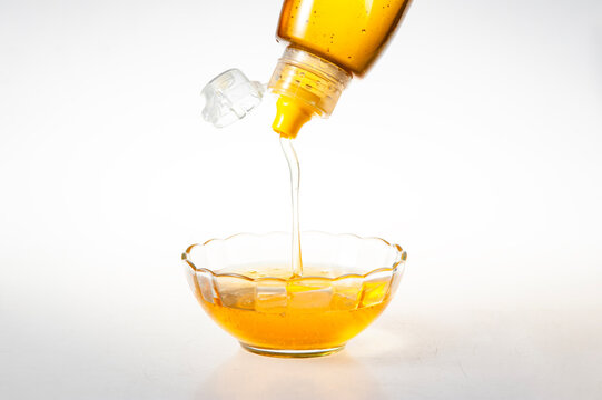 Golden Natural Honey Dripping from Squeeze Bottle into Clear Glass Bowl on Pure White Background