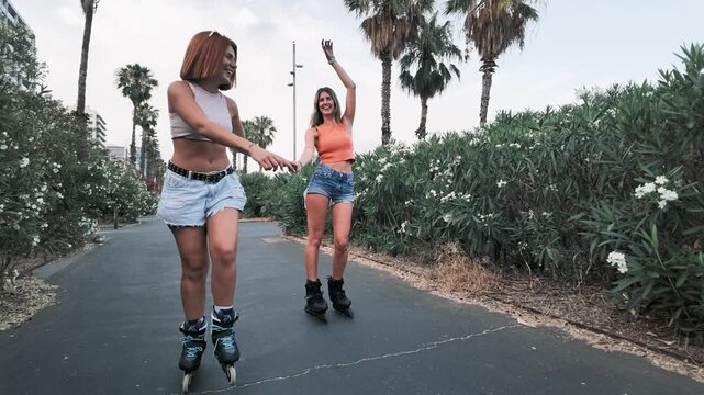 Two female friends rollerskating holding hands
