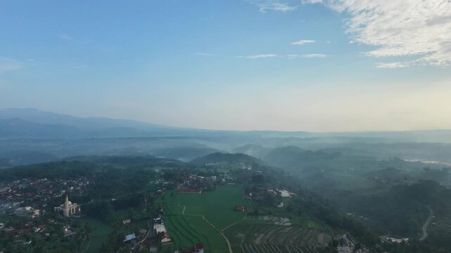 An aerial view captured by a drone showing mountains and settlements shrouded in cool morning fog in the Garut region of Indonesia