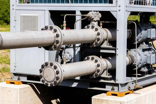 Industrial chiller unit with metal piping and bolted flanges on a concrete foundation outdoors