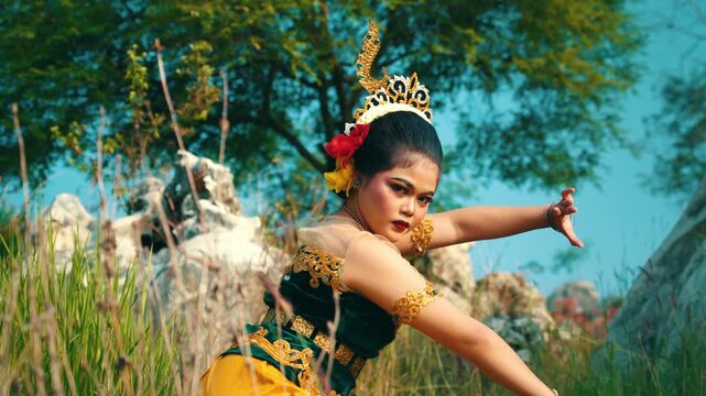 A traditional dancer performing intricate hand and arm movements while posing in tall wild grass, showcasing the beauty of Indonesian dance.
