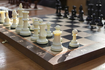 Wooden chessboard with white and black chess pieces aligned for a strategic game on a sunlit table. © PuzzleSoul