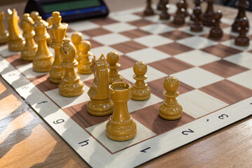 Wooden chess pieces and board beside a tournament chess clock on a sunny day in chess club. © PuzzleSoul