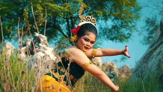 A stunning shot of a Javanese dancer posing dynamically surrounded by tall wild grass and limestone rocks, wearing a bright yellow and green outfit.
