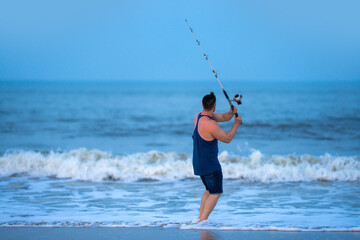 Fototapeta premium Sea fishing creates outdoor recreation. Sea fishing shows ocean lifestyle. Angler enjoys sea fishing on beach. Man practices sea fishing by surf.