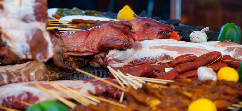 Traditional barbecue features roasted pig head. Grilled pork and sausages fill market. Rustic barbecue display attracts food lovers. Fresh meat selection suits gourmet cuisine.