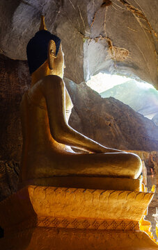 Golden Buddha statue seated inside Tham Hoi Cave near Vang Vieng, Laos, with natural light illuminating the limestone interior.