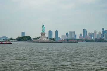 The Statue of Liberty stands on Liberty Island in New York Harbor with the modern skyline of New Jersey visible in the background. The famous monument symbolizes freedom and immigration in the United © DenisProduction.com