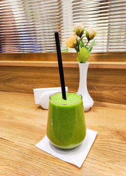Fresh green smoothie in glass with black straw on white napkin and wooden table. Healthy eating, detox and wellness lifestyle concept.