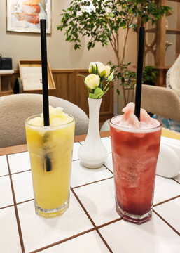 Two tall glasses with refreshing crushed ice drinks and fruit syrups on tiled table in cafe. Yellow and red slushies with black straws. Beverage, summer refreshment and gastronomy concept.