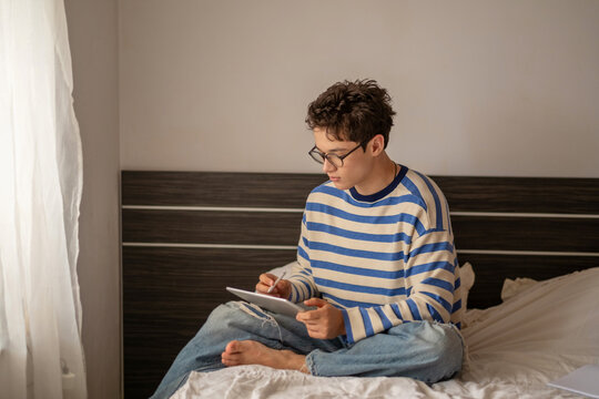Teenage boy drawing with stylus on graphic tablet, sketch made with thin digital pen, image made for honest content marketing. Wide shot. Concept of digital drawing on tablet at home