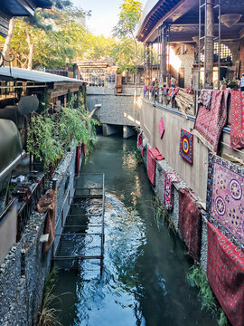 Colorful carpets hanging on walls near a narrow urban canal in Uzbekistan. Traditional architecture and a metal walkway over the water. Carpet washing and cultural heritage tourism background.