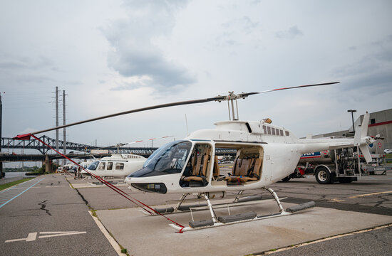 A modern white helicopter sits on a concrete heliport ready for passenger flights. The aircraft is prepared for urban sightseeing helicopter tours near a city bridge.