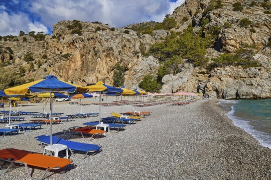 Pebble beach with colourful sun loungers and parasols, surrounded by rocky cliffs, Ahata Beach, Ahata, East Coast, Karpathos, Dodecanese, Greek Islands, Greece