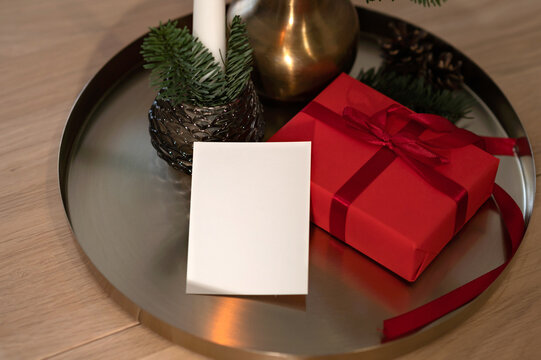 Christmas holiday card or invitation mockup, empty paper card and red present box, fir branches and candle on background, lifestyle