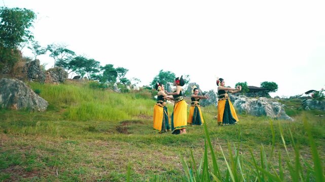 A group of Indonesian dancers in matching green and yellow costumes performing in a lined formation on a grassy hill.