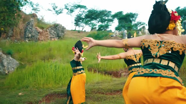A cinematic rear view of a group of Indonesian dancers in matching yellow and green costumes performing synchronized movements while moving away.