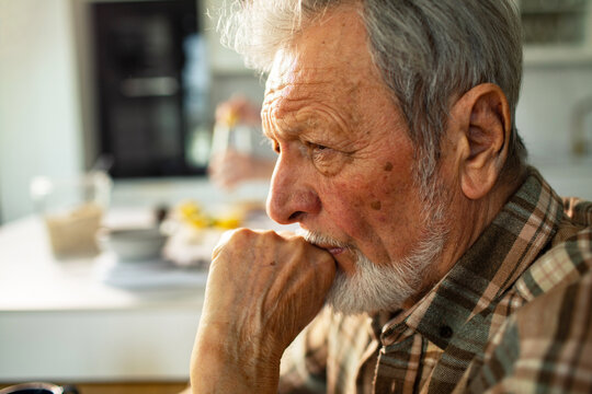 Thoughtful senior man resting chin on hand at kitchen table