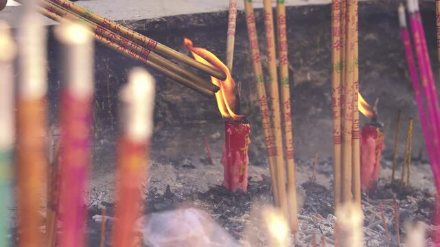 Burning incense sticks and red candles on temple altar with flames and ash