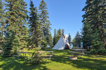 White Indigenous-Style Tipi Among Evergreen Trees Under a Clear Blue Sky in Prince Albert National Park, Canada. © Jolanta