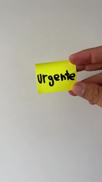 Hand holding spanish urgent sticky note on white background