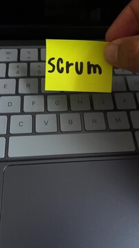 Hand holding scrum sticky note over laptop keyboard