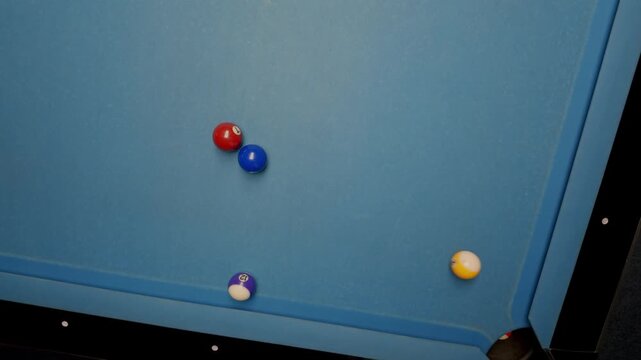 Player's hand holding a cue stick breaking a group of colored balls on a blue felt pool table during a game of billiards, with balls scattering across the surface after the impact