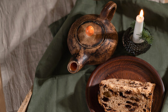 Crafted clay teapot, panettone cake and lighting candle on green linen napkin, traditional homemade sweet bakery, rustic cottage table setting for dinner or breakfast