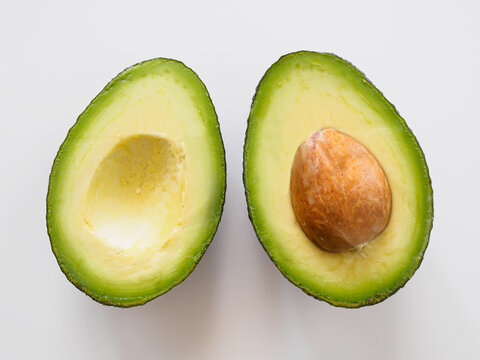 Close-up of ripe avocado cut in half showing creamy flesh, green skin and brown pit on white background