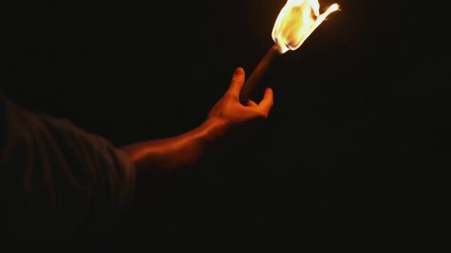 Hand Holds a Burning Torch Against a Dark Background as the Flame Flickers