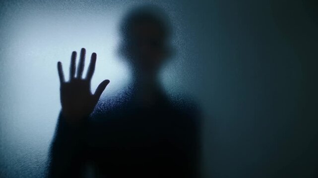 Silhouette of Person Pressing an Open Hand Against Frosted Glass in Blue Light