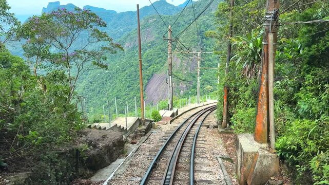 Mountain railway descends through tropical forest on Corcovado in Rio, Parallel steel tracks lead toward distant city views beneath green vegetation