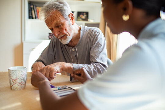 Caregiver helping senior man check blood sugar at home