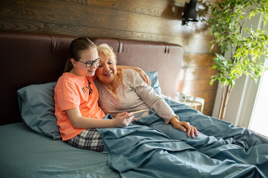 Girl showing smartphone to grandmother in bed